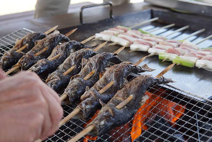 バーベキューで炭火で焼かれる串付きのイワナ