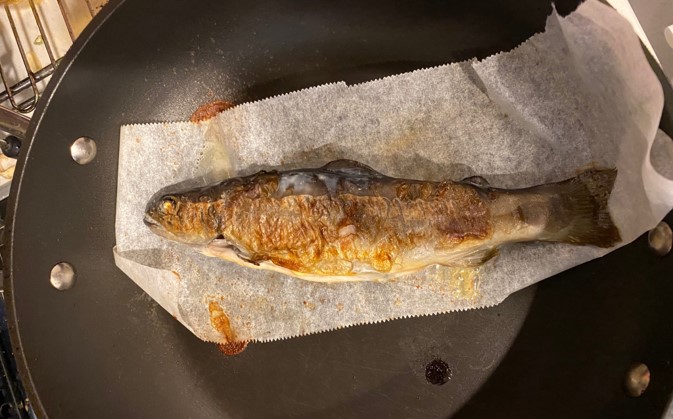フライパンでクッキングシートを敷いて焼かれるイワナ
