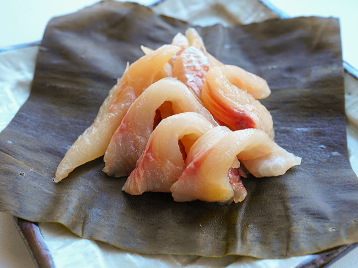 薄く切った昆布〆の刺身を木の皿に盛り付け、日本酒と合わせている写真